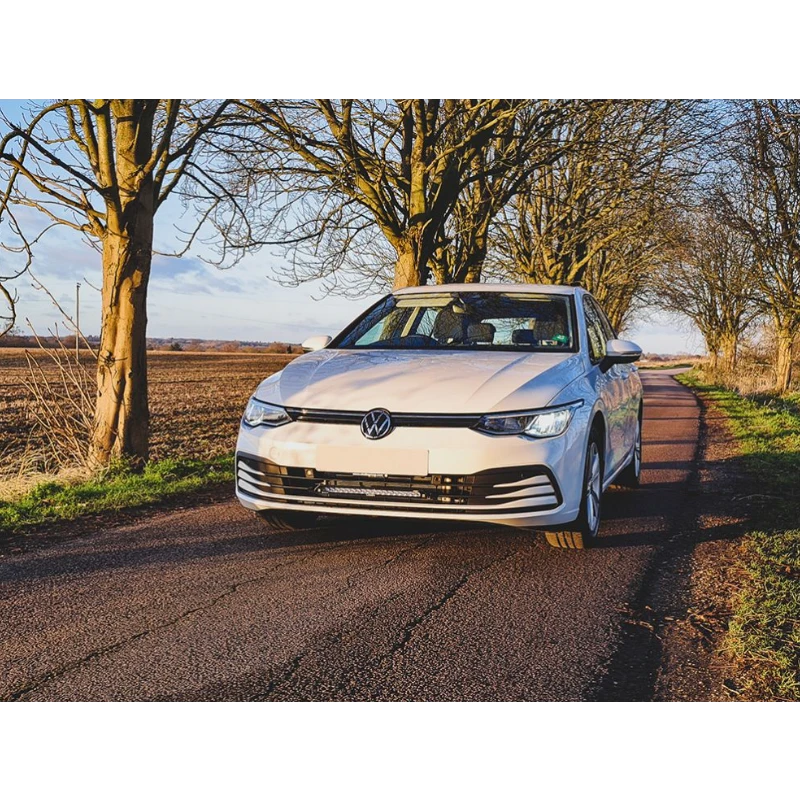 White Volkswagen car on a rural road with trees and fields in the background with Lazer Lamps Grille Kit for VW Golf MK8 (2020–2024)