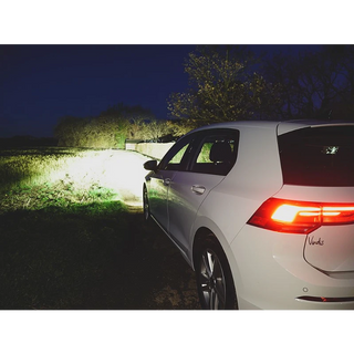 White car parked on a grassy area at night with visible brand logo.