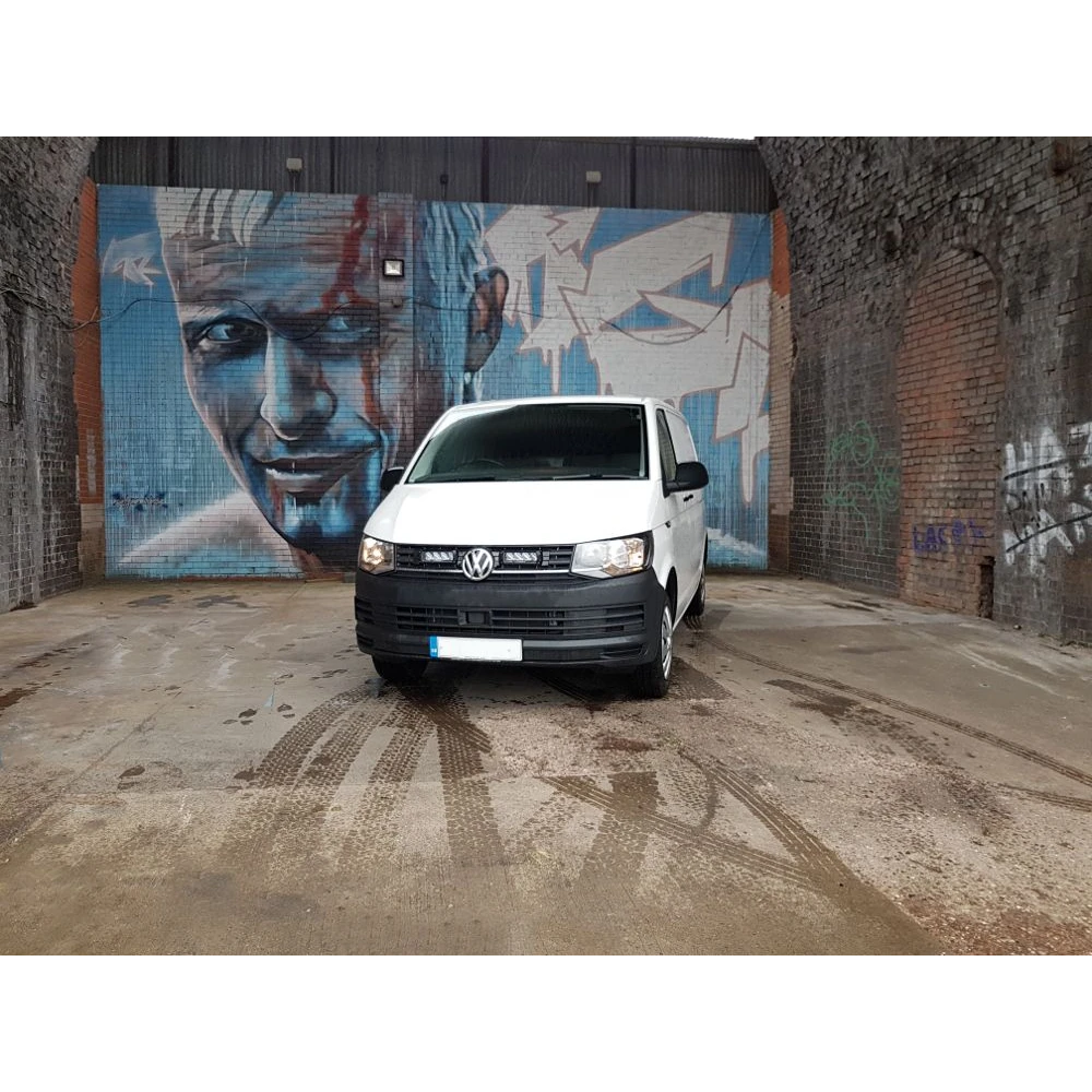 White van parked in front of a mural on a brick wall.