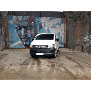 White van parked in front of a mural on a brick wall.