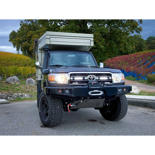 Black Toyota truck with a camper shell on a road with trees and colorful fields in the background