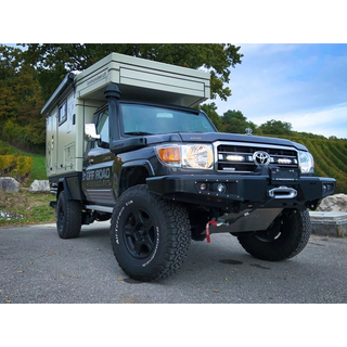 Toyota truck with a camper shell parked on a road with trees in the background