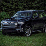 Black Toyota 300 series parked on grass with trees in the background