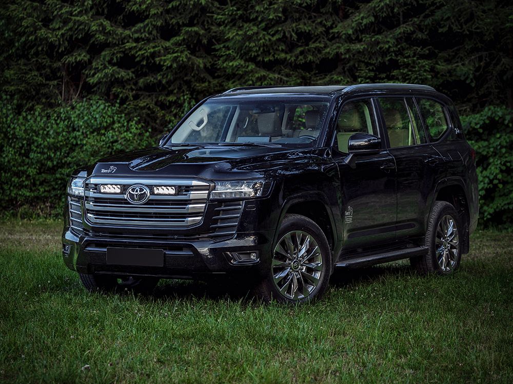 Black Toyota 300 series parked on grass with trees in the background