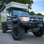 Toyota truck with a camper shell parked on a road with trees in the background