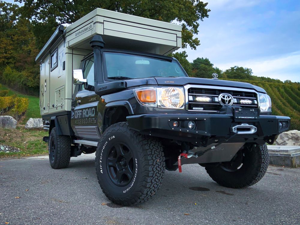 Toyota truck with a camper shell parked on a road with trees in the background