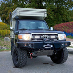 Black Toyota truck with a camper shell on a road with trees and colorful fields in the background