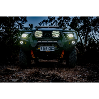 Front view of a green Mazda BT-50 at dusk with a pair of Lightforce BEAST driving lights illuminated on the bullbar