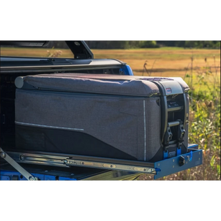 A fridge in its padded grey cover strapped to an MSA slide, pulled out over the tailgate of a ute with a paddock behind