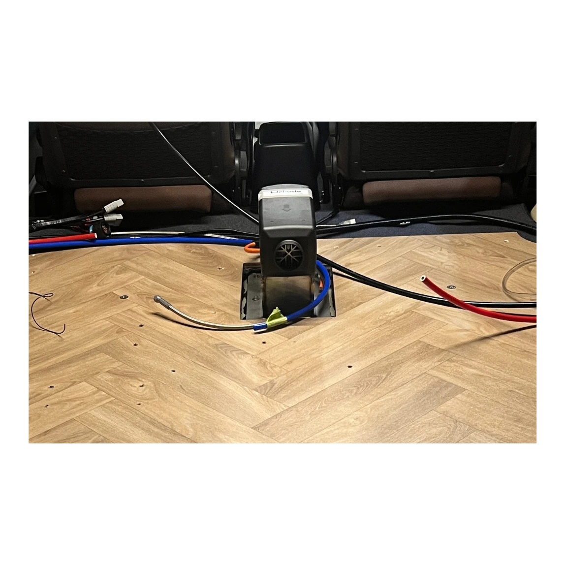 Car interior with wiring and a diesel heater on a wooden floor.