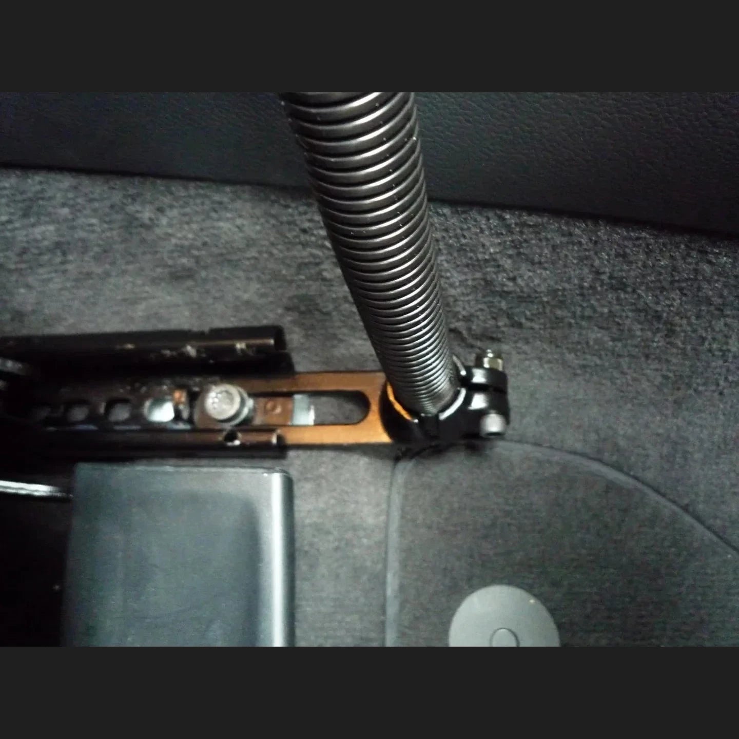 RAM floor mount installed in a vehicle footwell, the black base plate bolted through the carpet to the seat rail with the flexible aluminium rod rising from the ball clamp