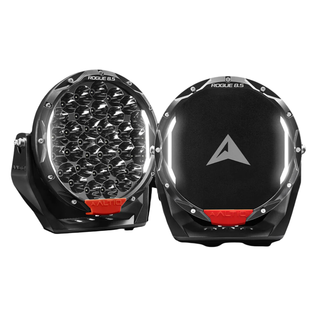 A pair of ALTIQ Rogue 8.5 driving lights side by side, one showing the reflector face with its dense cluster of LEDs and the ROGUE 8.5 marking on the bezel, the other fitted with a black cover carrying the ALTIQ arrow, both with red ALTIQ trim tabs at the base