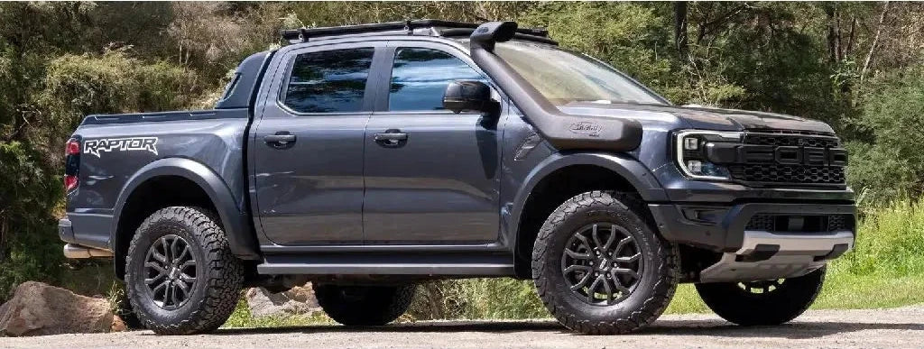 Gray Ford Raptor truck on a road with trees in the background