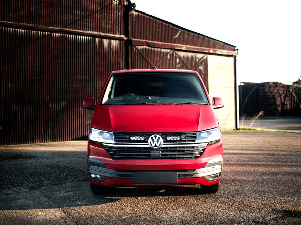 Red Volkswagen van parked in front of a rustic building.