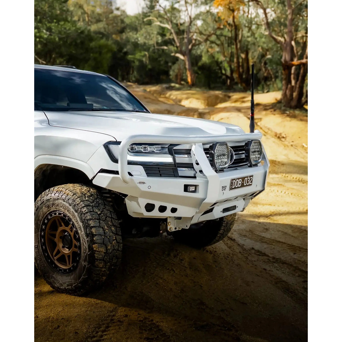 White off-road vehicle on a dirt road with trees in the background – TCC Toyota LandCruiser 300 Series Bull Bar