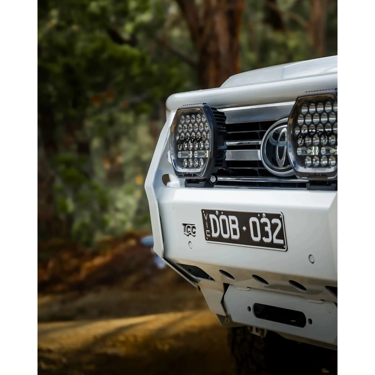 Close-up of a white Toyota vehicle's front bumper with LED lights and a blurred natural background – TCC Toyota LandCruiser 300 Series Bull Bar