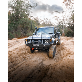 Off-road vehicle driving on a muddy path with trees in the background – TCC 70 Series Bull Bar - Facelift (2024 - Present)