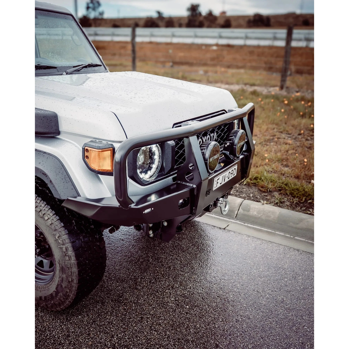 White off-road vehicle on a road with a rural landscape in the background – TCC 70 Series Single Cab Bull Bar - Facelift (2024 - Present)