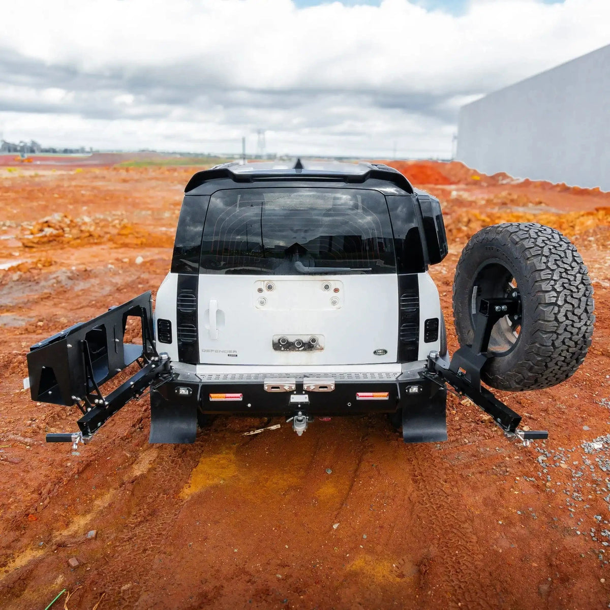 Back view of a vehicle with a spare tire and recovery winch on a dirt surface – TCC Land Rover Defender 2020+ Rear Bar