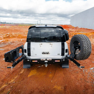 Back view of a vehicle with a spare tire and recovery winch on a dirt surface – TCC Land Rover Defender 2020+ Rear Bar