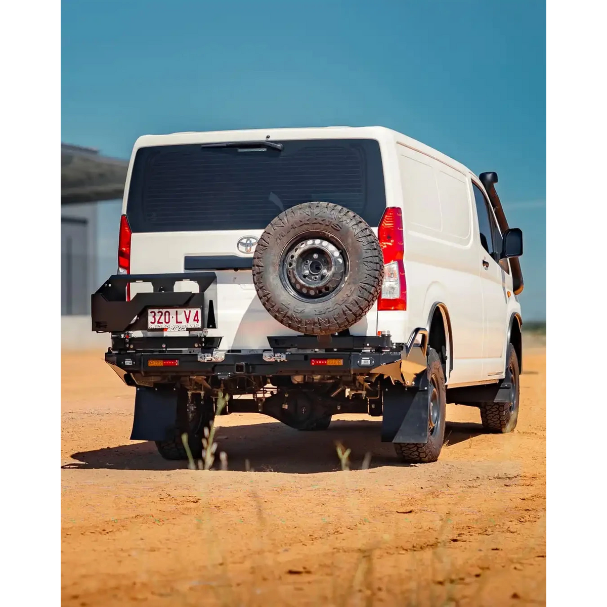 White van with a spare tire mounted on the back, parked on a dirt road – TCC Toyota Hiace 300 Series Rear Bar