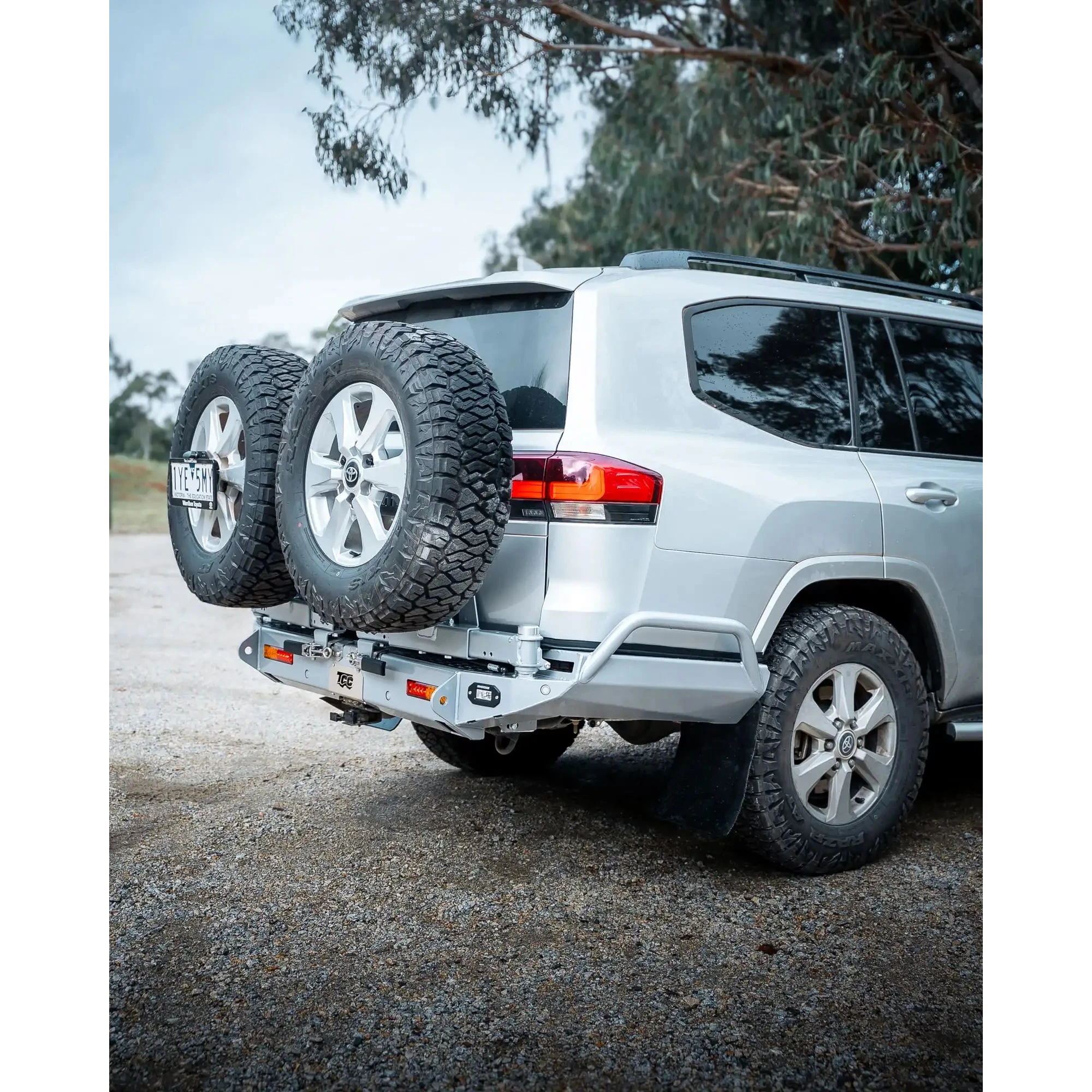 Silver SUV with a spare tire on a hitch, parked outdoors with trees in the background – TCC Toyota LC300 Series Rear Bar