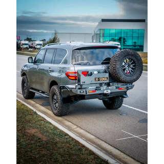 Silver SUV with off-road tires on a road near a building – TCC Y62 Patrol Rear Bar