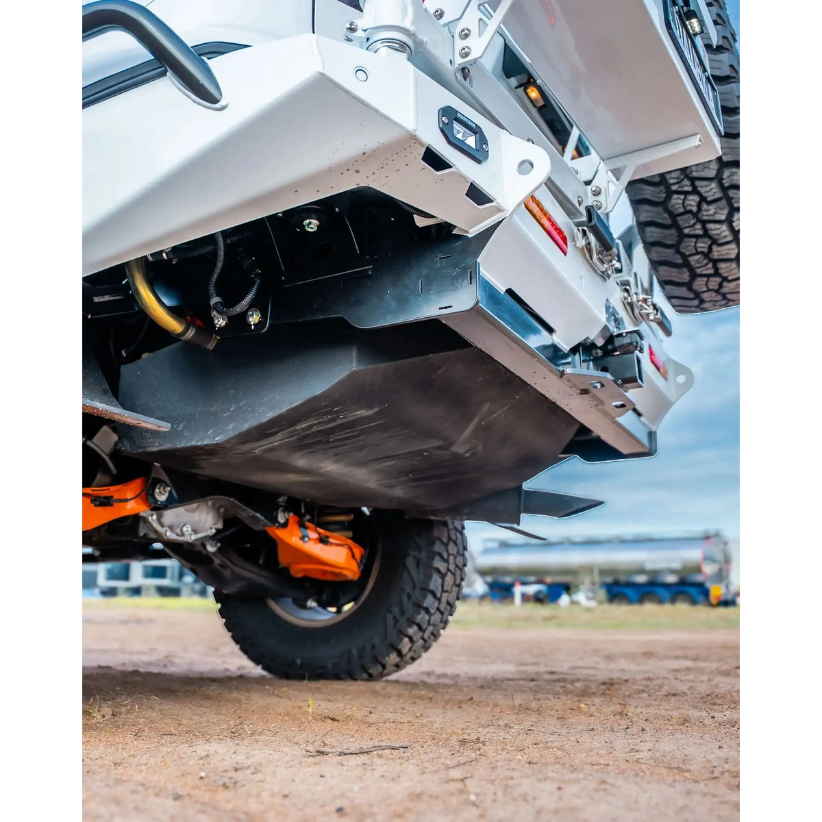 Close-up of a vehicle's undercarriage with visible suspension and tires on a dirt surface – TCC Y62 Patrol Rear Bar