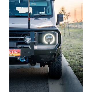 Front view of a white off-road vehicle with glowing headlights on a grassy area – TCC Ineos Grenadier Bull Bar