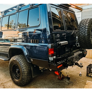 Blue off-road vehicle with large tires and Thorburns LC75/78 Rear Bar on a concrete surface.