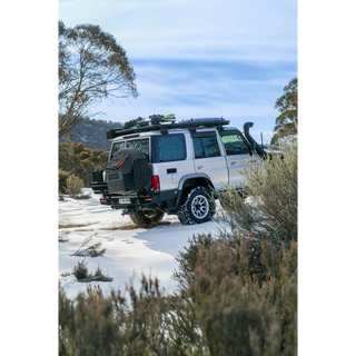4x4 vehicle on a snowy road with trees and mountains in the background – Thorburns LC76 Rear Bar