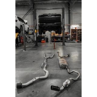Exhaust system on the floor of a garage with a vehicle on a lift in the background – Torqit 3″ CAT Back Performance EXHAUST Toyota Tundra 3.5L V6 Petrol