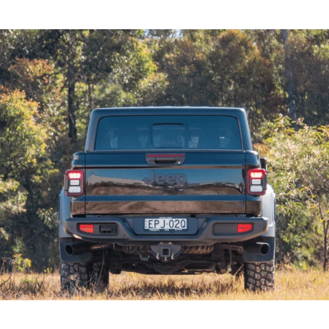 Back view of a black Jeep truck in a natural setting with trees and grass.