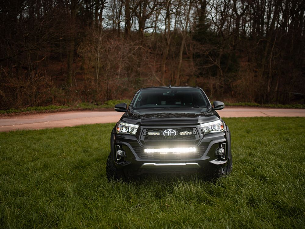 Black Toyota truck with headlights on in a grassy area with trees in the background