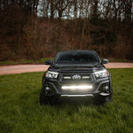 Black Toyota truck with headlights on in a grassy area with trees in the background