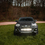 Black Toyota truck with headlights on in a grassy area with trees in the background