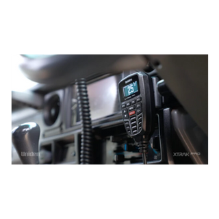 A Uniden XTRAK Pro UHF controller mounted in a vehicle cab, the backlit screen showing channel 25, with the coiled microphone lead running down beside the dash