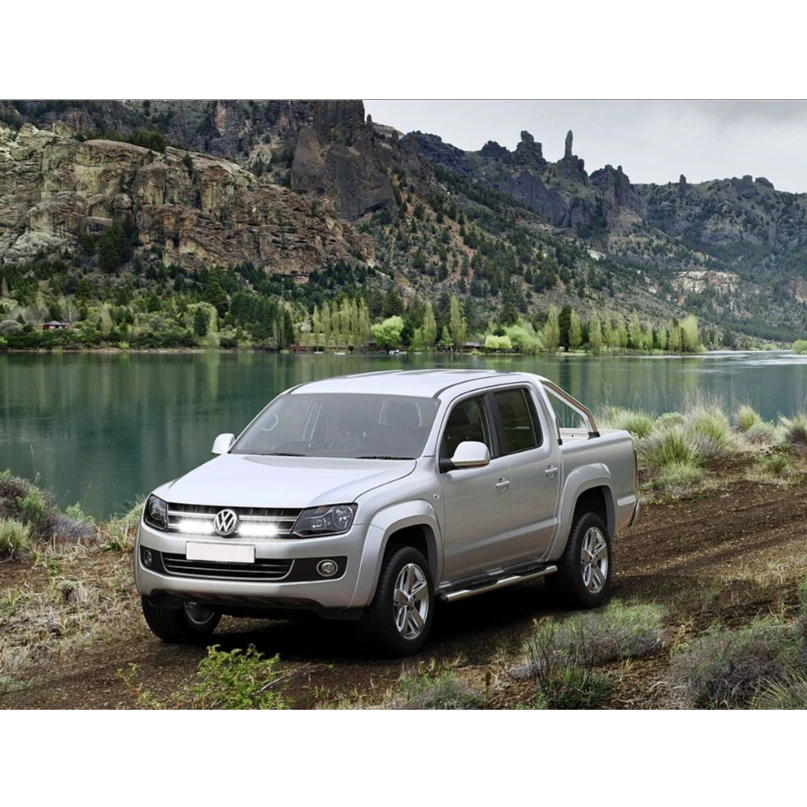 Silver Volkswagen Amarok parked on a dirt road with a scenic mountain and lake background