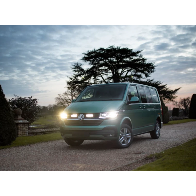 Green Volkswagen van on a gravel driveway with trees and a cloudy sky in the background