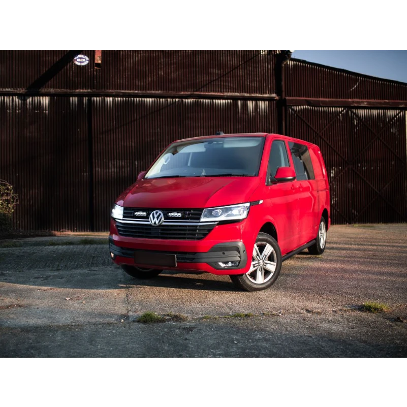 Red Volkswagen van parked in front of a rustic metal building.