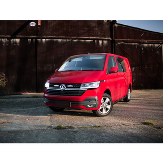 Red Volkswagen van parked in front of a rustic metal building.