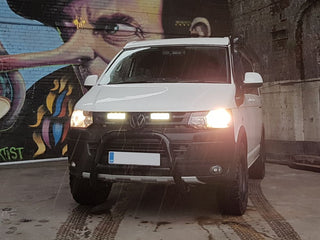 White Volkswagen van with headlights on in front of a colorful mural with Lazer Lamps Grille Kit for Volkswagen T5.1