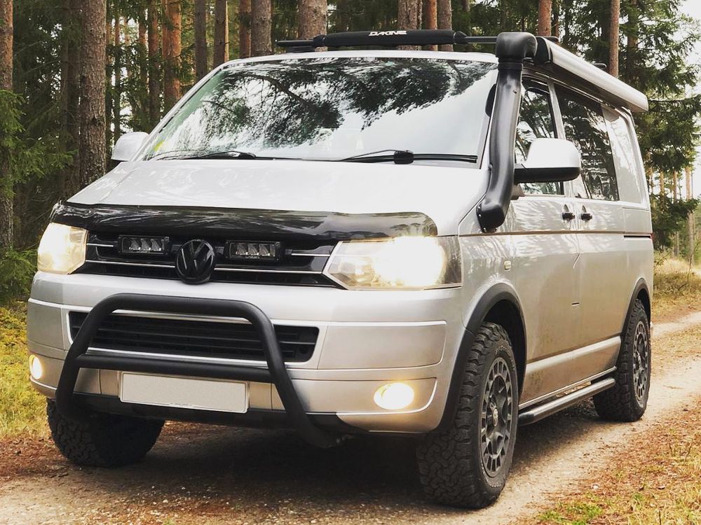 White van with roof rack and off-road bumper in a forest setting