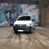 White van parked in front of a mural on a brick wall.